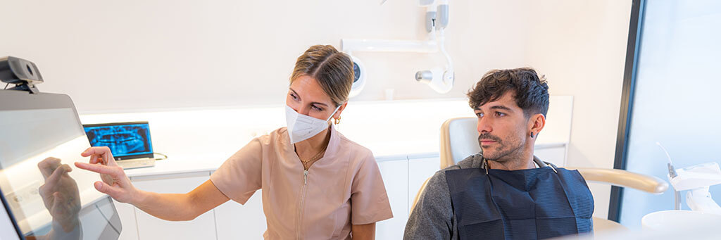 Zahnmedizinische Fachangestellte zeigt Patienten etwas auf Bildschirm